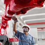 Male workers spray painting a crane arm red in factory workshop, China